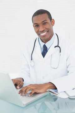 Smiling doctor using laptop at medical office