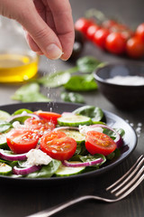 hand adding salt to vegetable salad