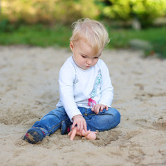 Cute baby girl playing in the playground sitting in the sand 
