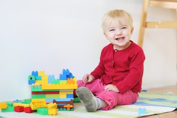 Funny baby girl playing indoors with colorful blocks