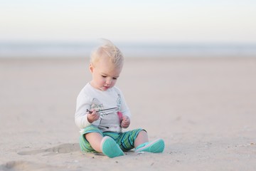 Little cute baby girl plays with sand on the beach