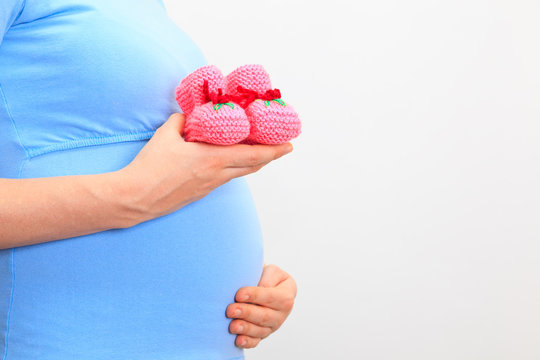 Pregnant woman holding pink baby shoes on her belly