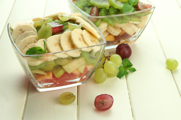 Tasty fruit salad in glass bowls, on white wooden table