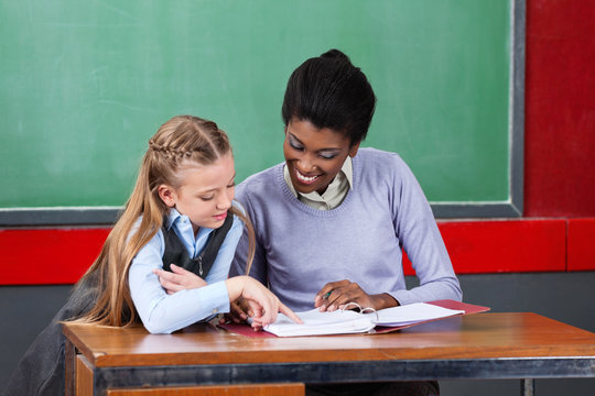 Teacher And Schoolgirl Reading Together At Desk
