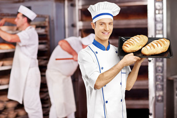 Smiling male baker posing with freshly baked breads in bakery
