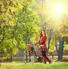 Fototapeta premium Young female with bicycle relaxing in a park on a sunny day