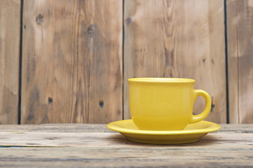 Fototapeta na wymiar Yellow coffee cup and saucer on a wooden table