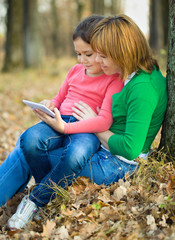 Mother is reading from tablet with her daughter