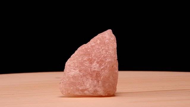 Rose quartz raw mineral stone revolves on the board