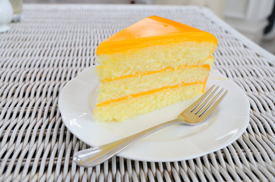 Orange Layer Cake On White Plate Put On Rattan Table.