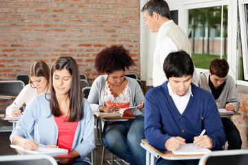Obraz premium Students Writing Exam While Teacher Supervising Them In Classroo