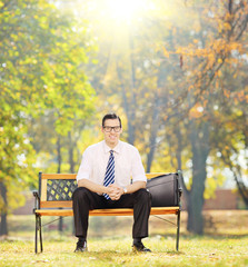 Relaxed businessman sitting on bench in a park on sunny day