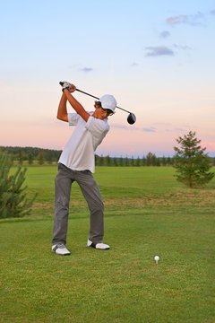 Golf, teenager golfer striking the ball at sunset