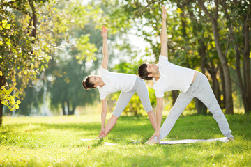 Couple Yoga, man and woman doing yoga exercises in the park - 58065387