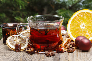 Glass of hot steaming tea among christmas decorations on wooden