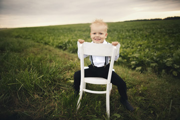 Naklejka na ściany i meble little boy sits on chair in the field