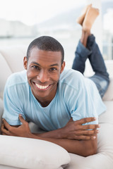 Relaxed smiling young Afro man lying on sofa