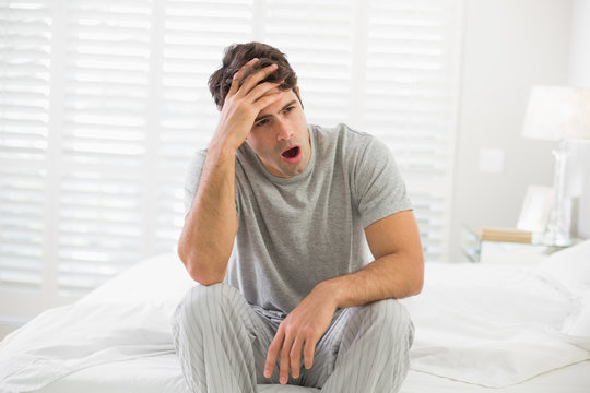 Sleepy Young Man Sitting And Yawning In Bed