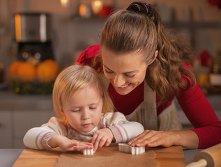 Naklejka premium Happy mother and baby cutting christmas cookies from dough