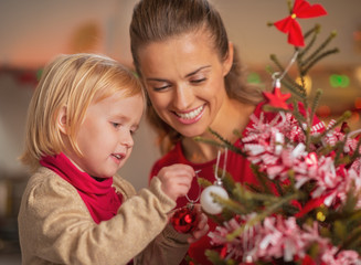 Baby helping mother decorate christmas tree
