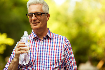 Fototapeta premium Smiling happy mature (old) man holding bottle of water
