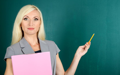 School teacher with folder near blackboard close-up