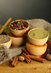 bowls and spoons with spices, on wooden table on grey