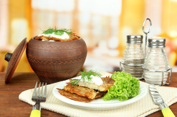 Potato pancakes in pot, on wooden table, on bright  background