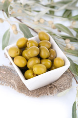 Olives in bowl with branch on sackcloth close up