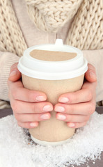 Hot drink in paper cup in hands with snow