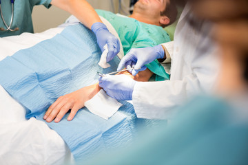 Doctor Stitching Patient's Wound While Nurse Assisting Him