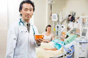 Doctor Holding Coffee Cup With Patient Resting In Hospital