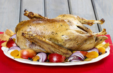 Roasted goose with apples and vegetables on wooden table.
