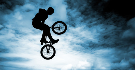 Man doing an jump with a bmx bike over blue sky background.