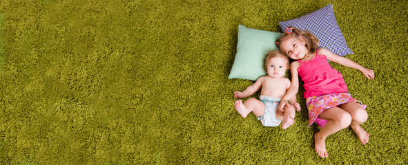 Two happy sisters lie on carpet