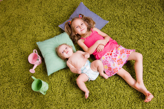 Two sisters lie on carpet