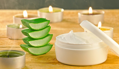 Fresh aloe vera slices and cream container on wooden.