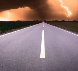 Driving on an empty road towards tornado and lightning