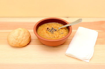 Lentil soup in a bowl with seasoning and bread roll