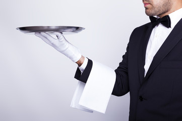 Professional waiter holding empty silver tray over gray backgrou