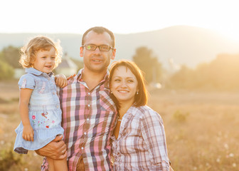 Fototapeta premium Happy mother, father and daughter in the mountains at sunset
