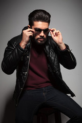Obraz premium bearded man in leather jacket is putting on his sunglasses