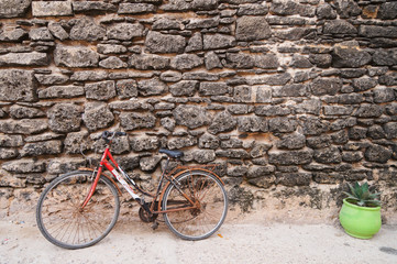 Fototapeta na wymiar Red bicycle and green pot at Mazagan Fortress wall, El-Jadida