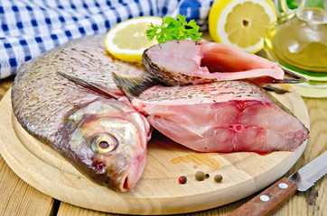 Bream raw on a round board with a knife and oil