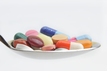 Many different colored tablets and pills on a spoon isolated in
