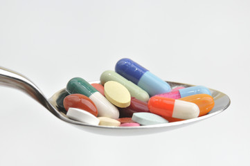 Many different colored tablets and pills on a spoon isolated in
