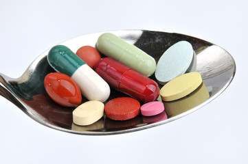 Many different colored tablets and pills on a spoon isolated in