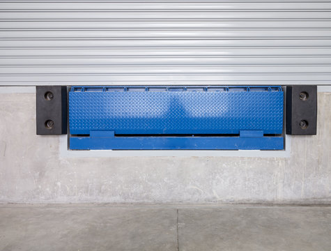 Dock leveler or height adjustable platform outside warehouse or industrial building. Used as bridge between dock and truck for loading, storage, warehousing, shipping and freight forwarding of cargo.