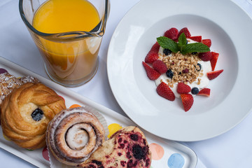 Strawberries, granola, blueberries, orange juice and pastries