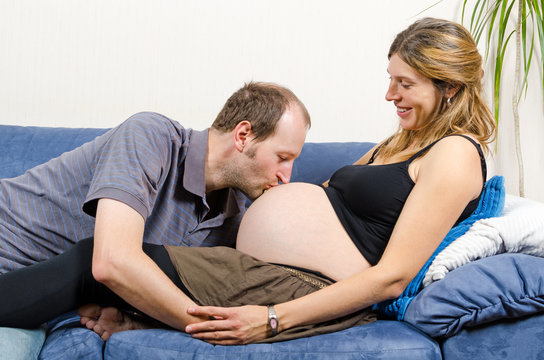 Happy husband kissing tummy of his pregnant wife on couch
